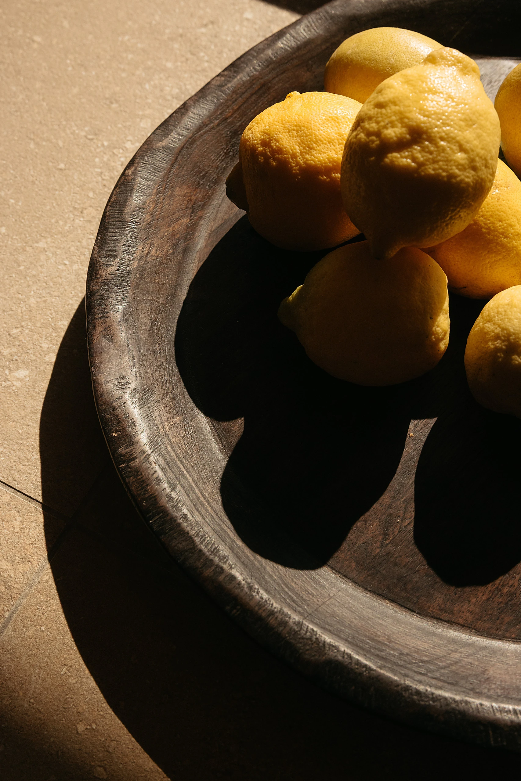 Lemons in a dark carved bowl, raking sunlight across the stone floor