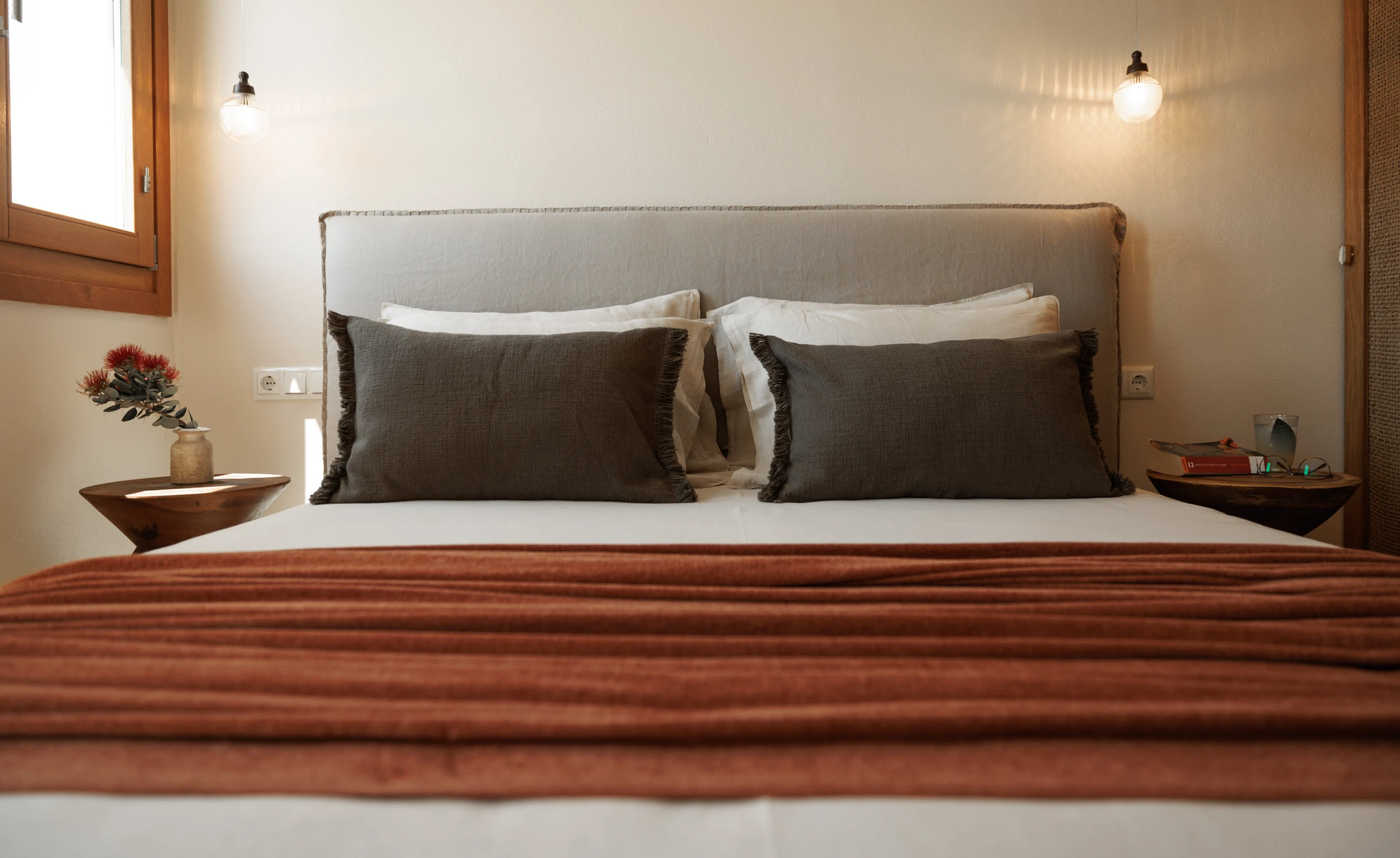 The bed seen head-on, grey fringed cushions and a ribbed terracotta throw