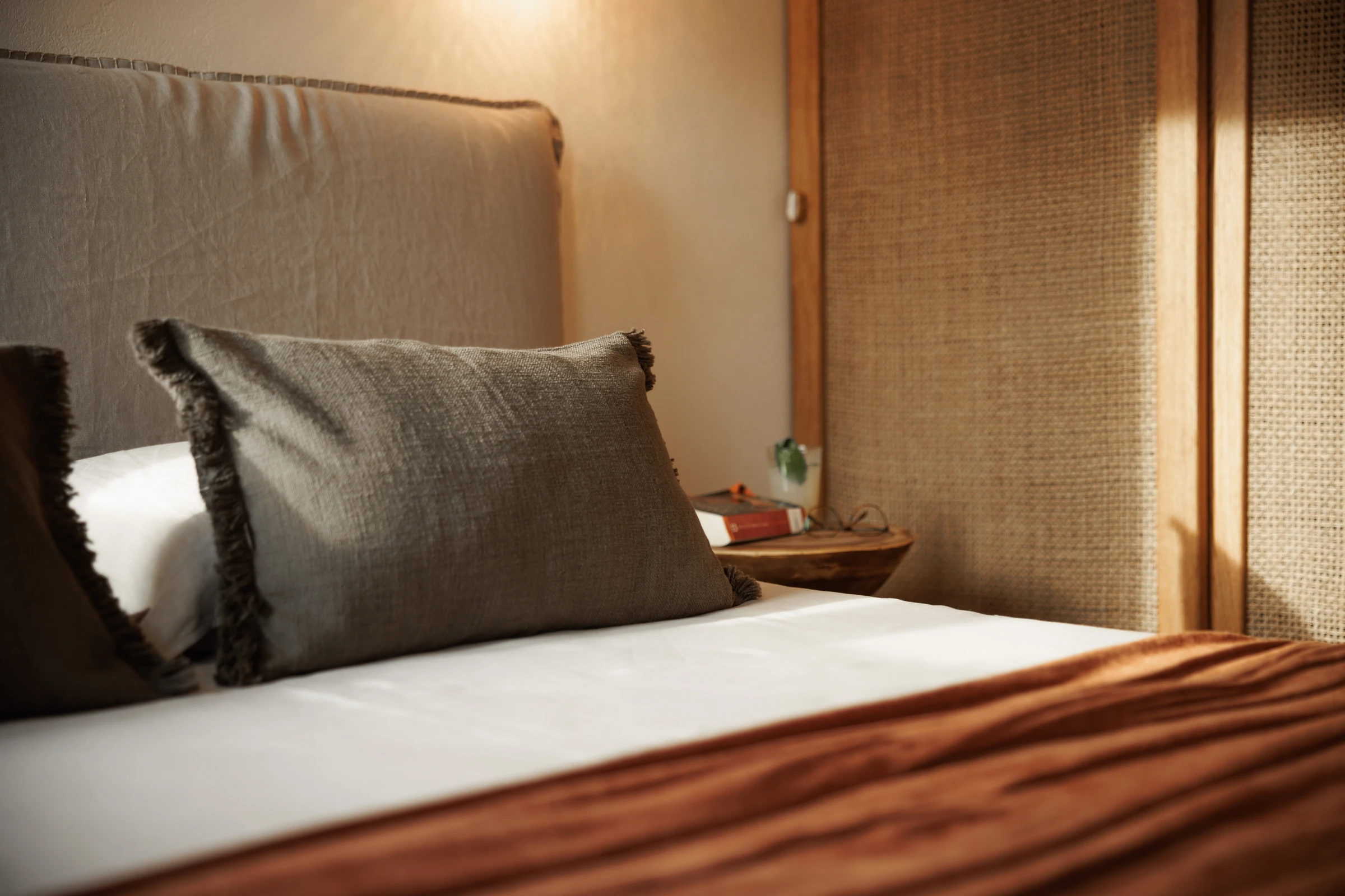 Low, raking light across the bed with the rattan wardrobe beyond