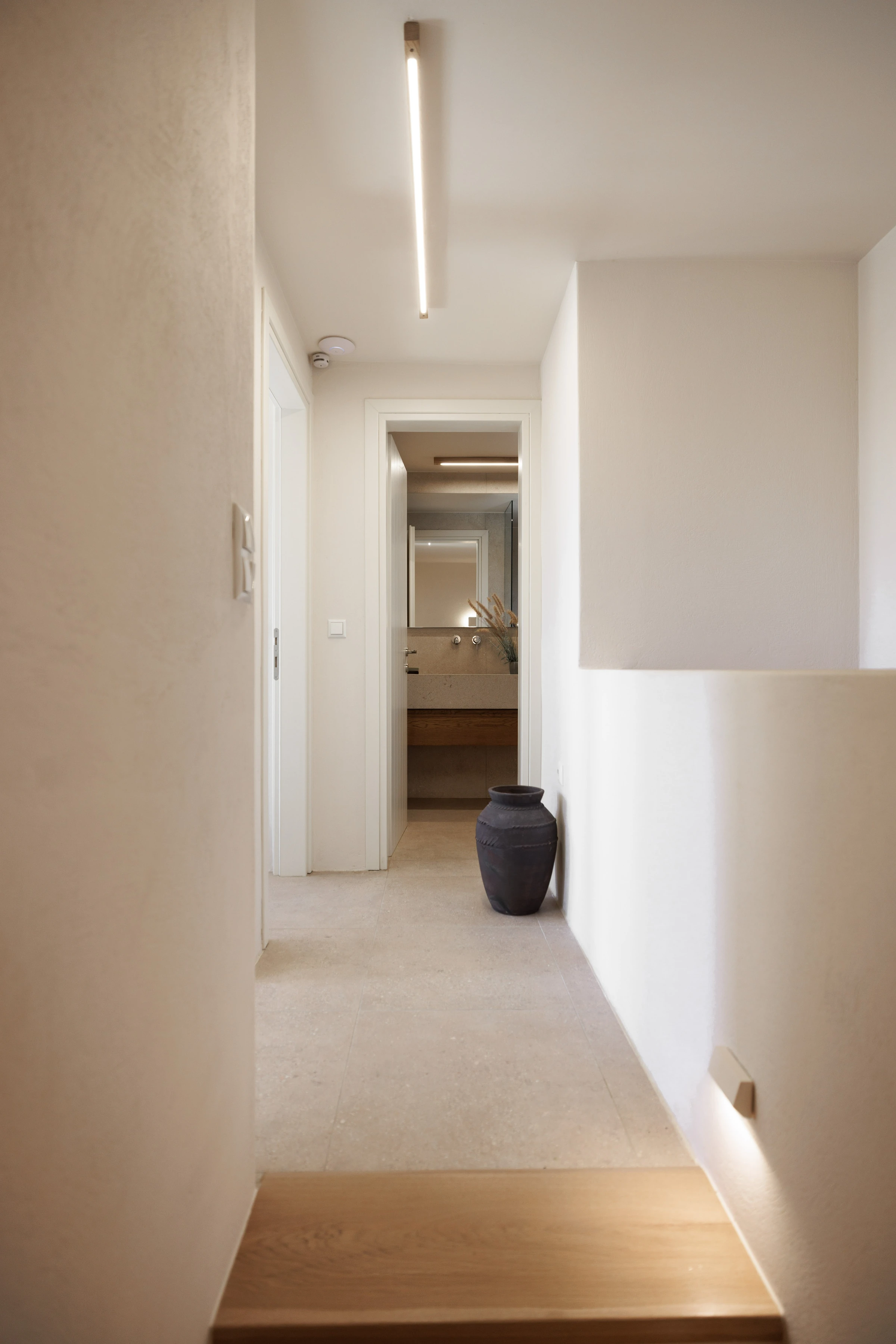 Hallway with a dark terracotta urn, looking through to the stone-basin bathroom