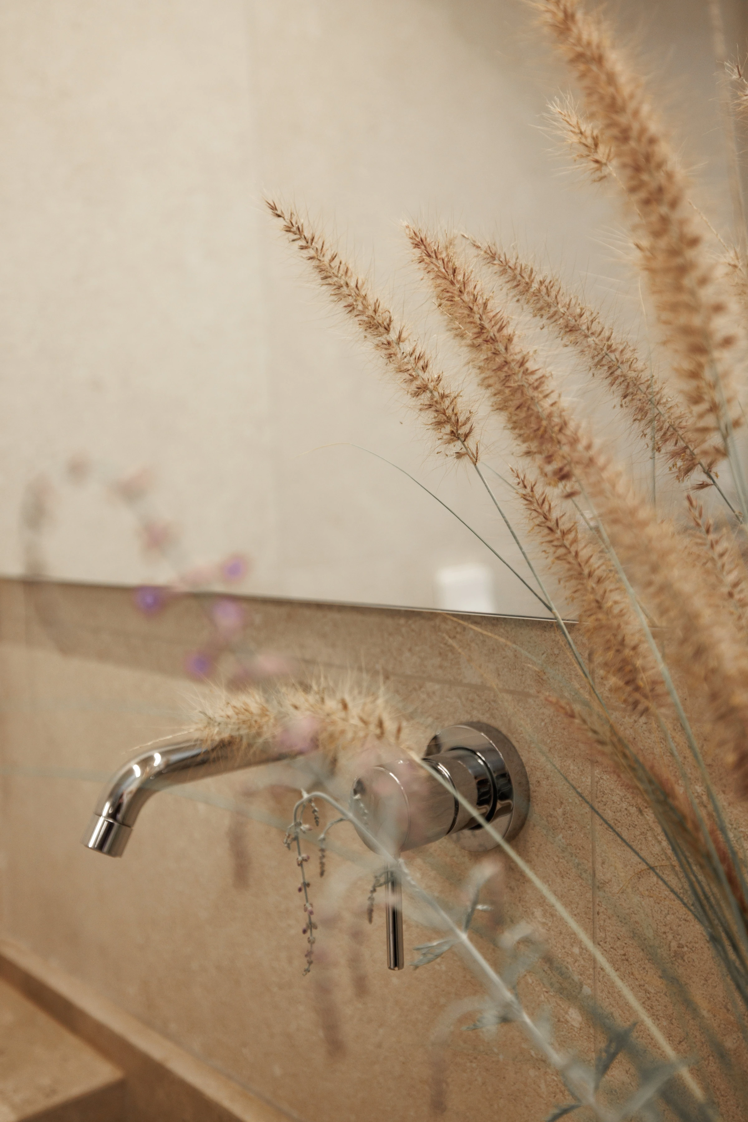 Wall-mounted tap and dried grasses at the stone basin