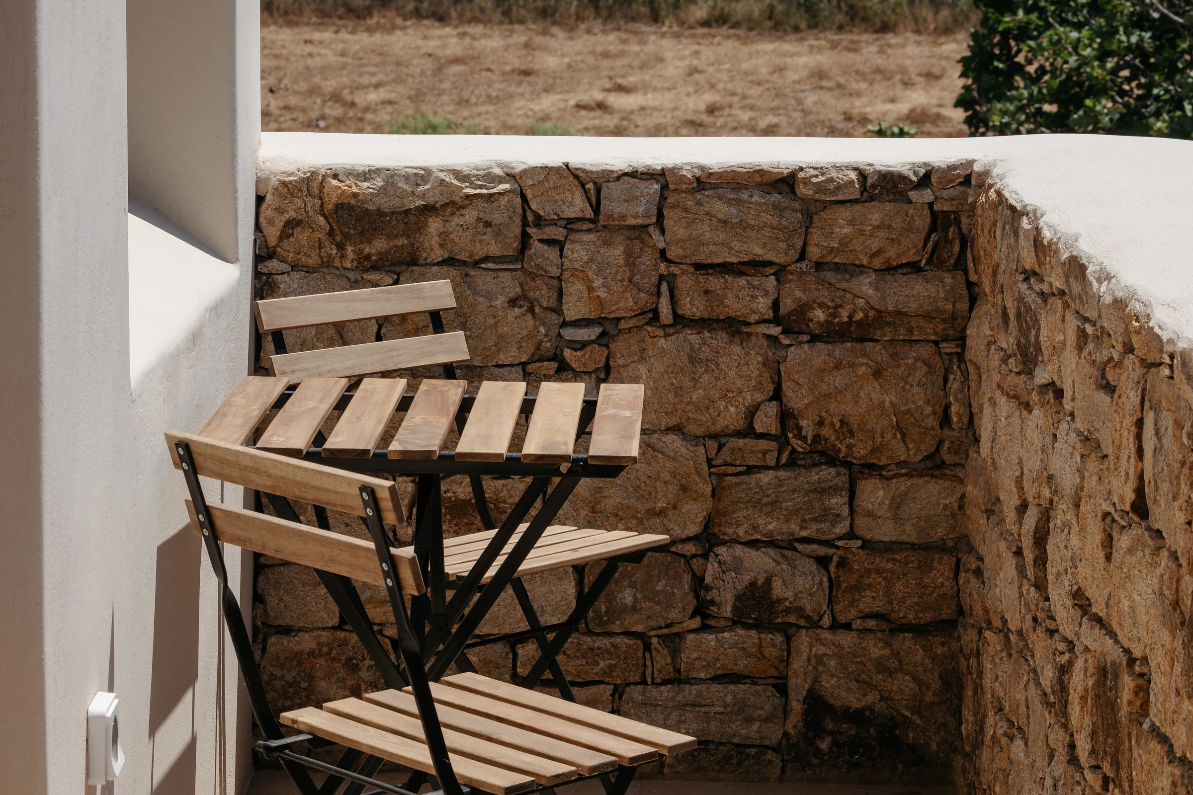 A folding timber bistro set against the dry-stone wall, dry fields beyond